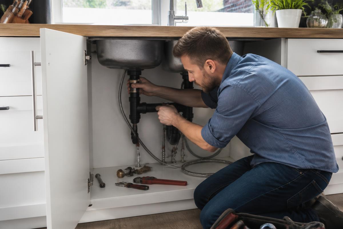 Plumber fixing a leaking drain pipe under a kitchen sink
